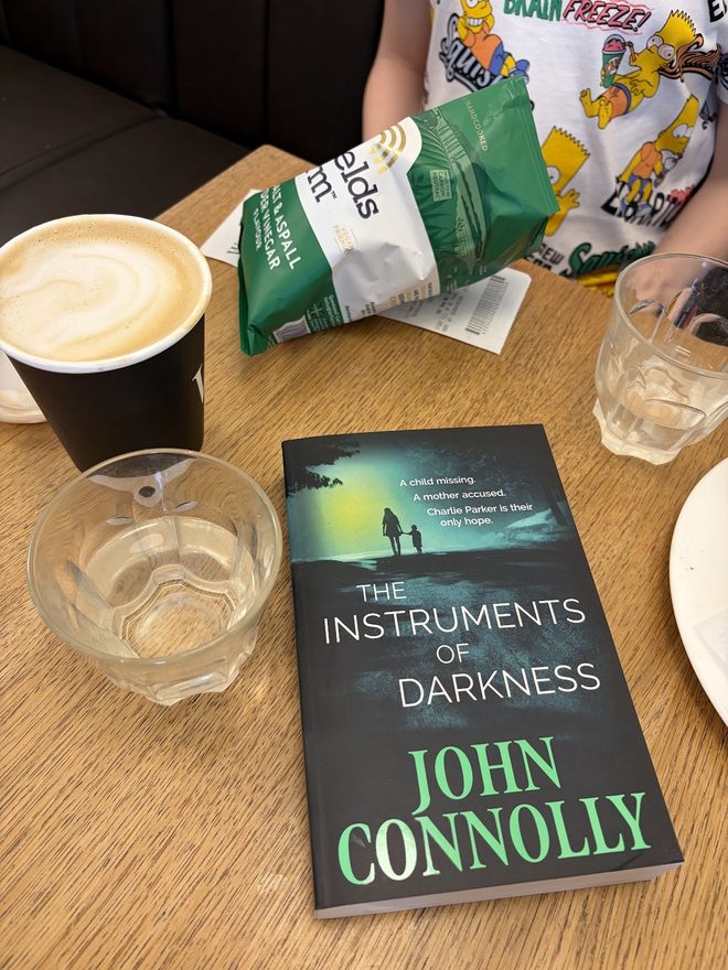 A paperback propped on a café table beside a coffee and a glass of water