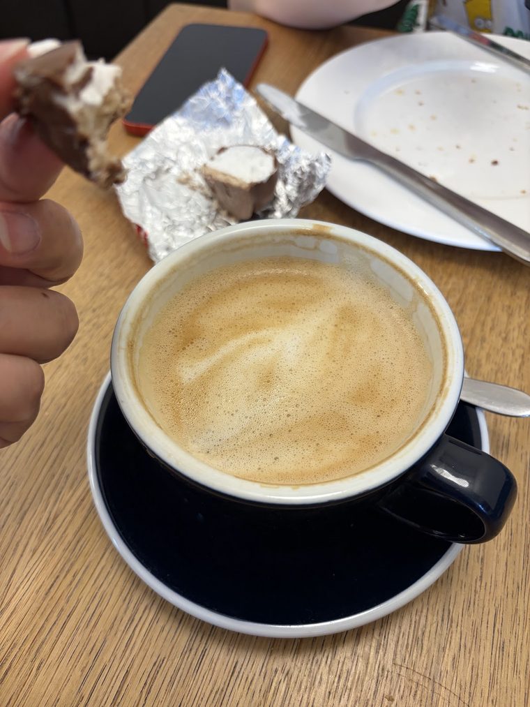 A large flat white in a black cup and saucer on a wooden table