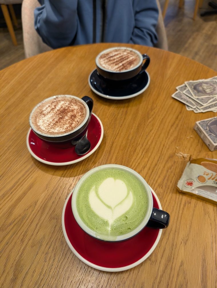 A matcha latte with a leaf pattern beside two coffees