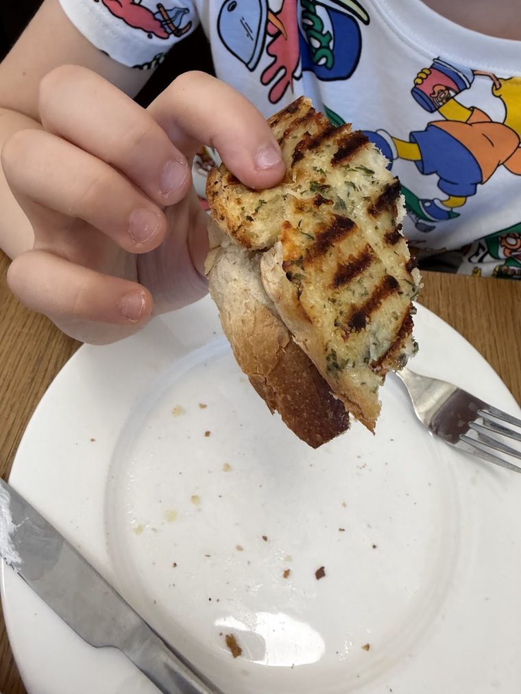 A toasted cheese panini, half eaten, being lifted from the plate
